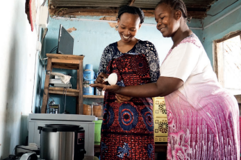 two women scooping food from pot