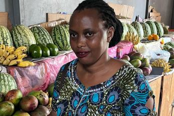Woman stands smiling, in front of table of fruit.